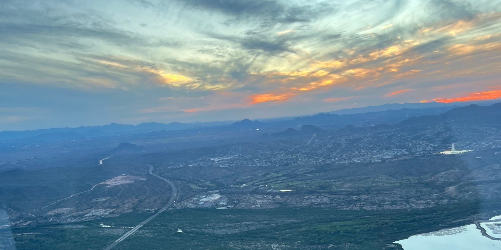 Sunset over the Valley from a small plane, with mountains on the horizon and desert below.